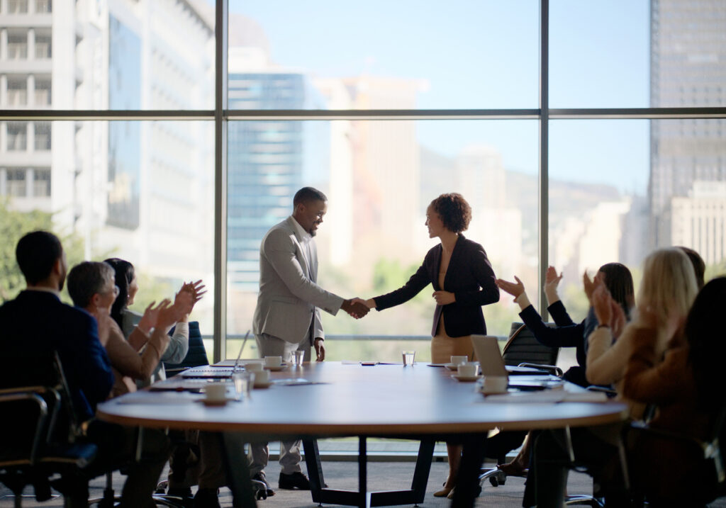Boardroom handshake in front of a large conference room window